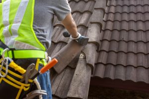 Professional roofer wearing safety gear inspects and replaces damaged roof tiles, restoring the old roof to top condition.