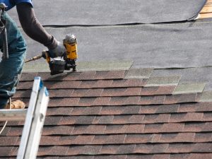 Worker installing shingles on a roof with a nail gun to prevent roof sagging caused by improper installation.