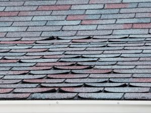 Roof with lifted shingles indicating potential roof sagging issues due to poor installation or material failure.